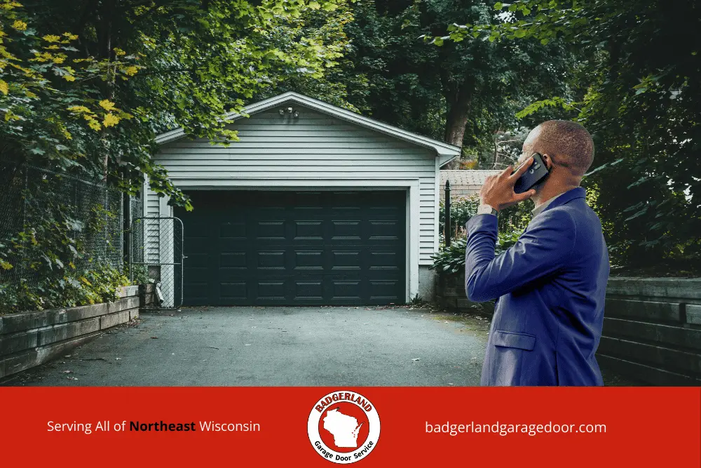 Why Garage Door Balance Matters More in Wisconsin Winters-3 A man in a blue suit talks on his phone in front of a closed garage door, possibly discussing Wisconsin garage door repair.| Bestland Garage Door Service – Green Bay & Appleton Garage Door Repair