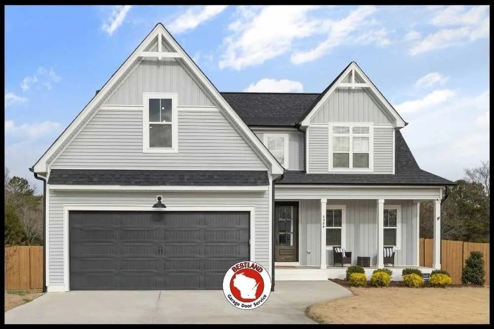 A modern gray house with a large black garage door, highlighted by a Bestland Garage Door Service logo, represents their professional garage door repair services…| Bestland Garage Door Service – Green Bay Garage Door Repair