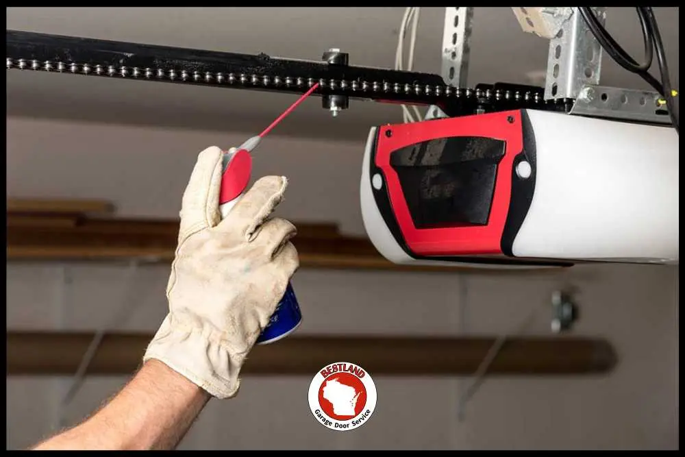 A gloved hand sprays lubricant on a garage door opener's chain, showcasing maintenance work. The image highlights Bestland Garage Door Service, a company known for garage door repair in Green Bay and Appleton.| Bestland Garage Door Service – Green Bay Garage Door Repair