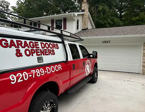 A red service truck with "Garage Doors & Openers" signage is parked in front of a house with a white garage door in a residential area, illustrating a garage door repair service available in Green Bay and Appleton.| Bestland Garage Door Service – Green Bay Garage Door Repair