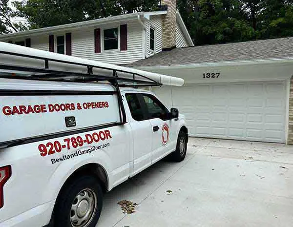 A white service van from Bestland Garage Door Service is parked in front of a suburban home in Green Bay, showcasing their garage door repair services. The house has a two-car garage with the number 1327 above the door.| Bestland Garage Door Service – Green Bay Garage Door Repair