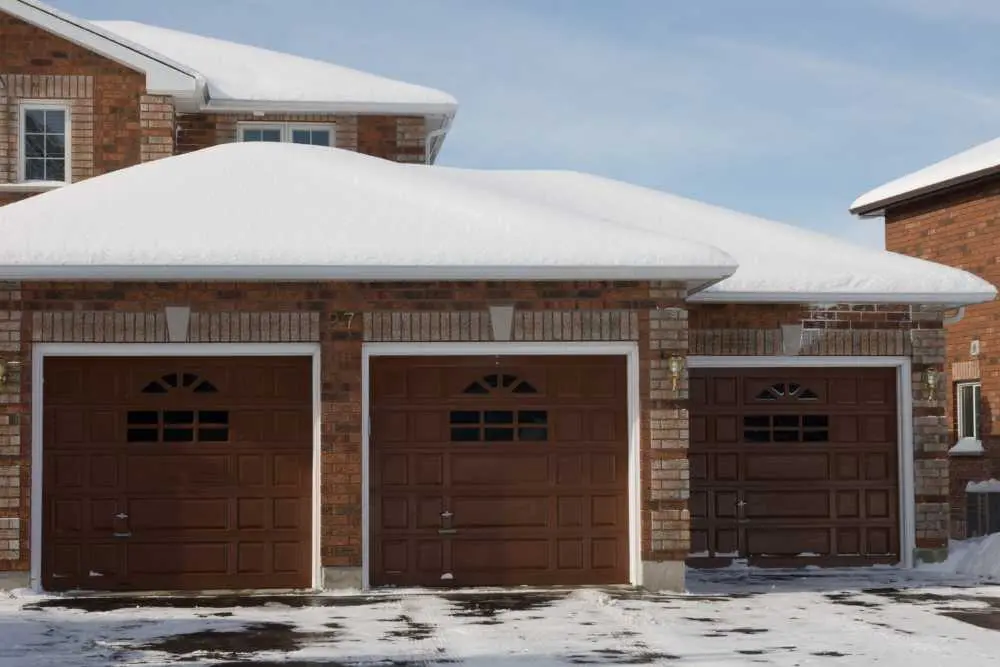 A snow-covered house in Green Bay with three brown garage doors showcases the need for reliable garage door repair services. The brick exterior adds a classic touch, emphasizing the importance of maintenance in harsh weather conditions.| Bestland Garage Door Service – Green Bay Garage Door Repair