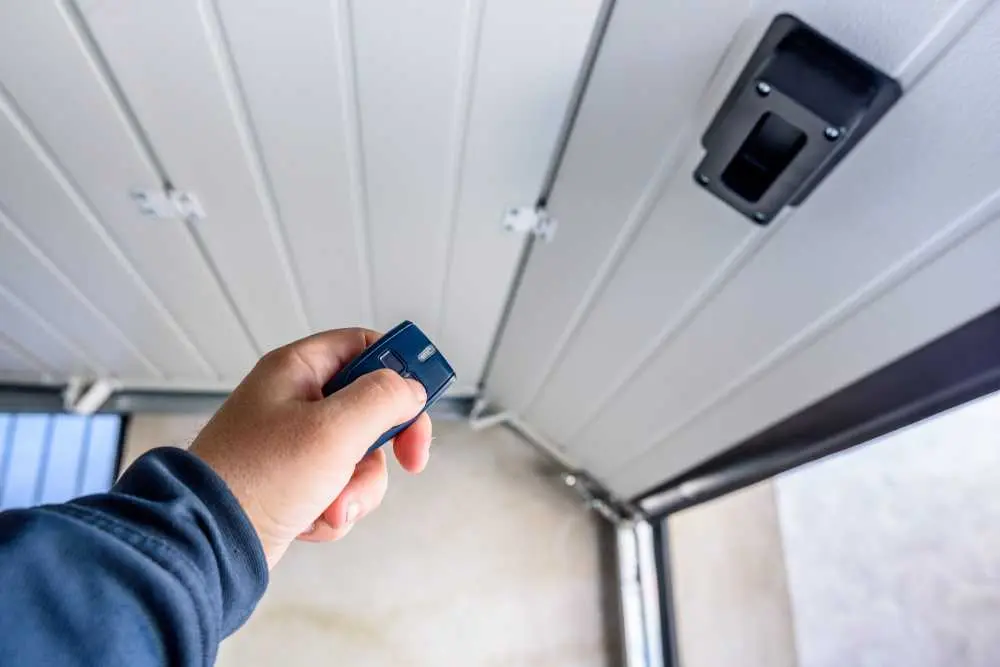 A hand holding a remote control is pointed at a partially open garage door, highlighting the convenience of modern garage door systems. This scene emphasizes the importance of professional garage door repair services in Green Bay and Appleton.| Bestland Garage Door Service – Green Bay Garage Door Repair