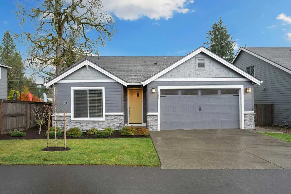 A modern gray house with a two-car garage, lawn, and a tree in the front yard. The home exemplifies a typical suburban style found in Green Bay. Ideal for showcasing garage door repair services offered in the area.| Bestland Garage Door Service – Green Bay Garage Door Repair