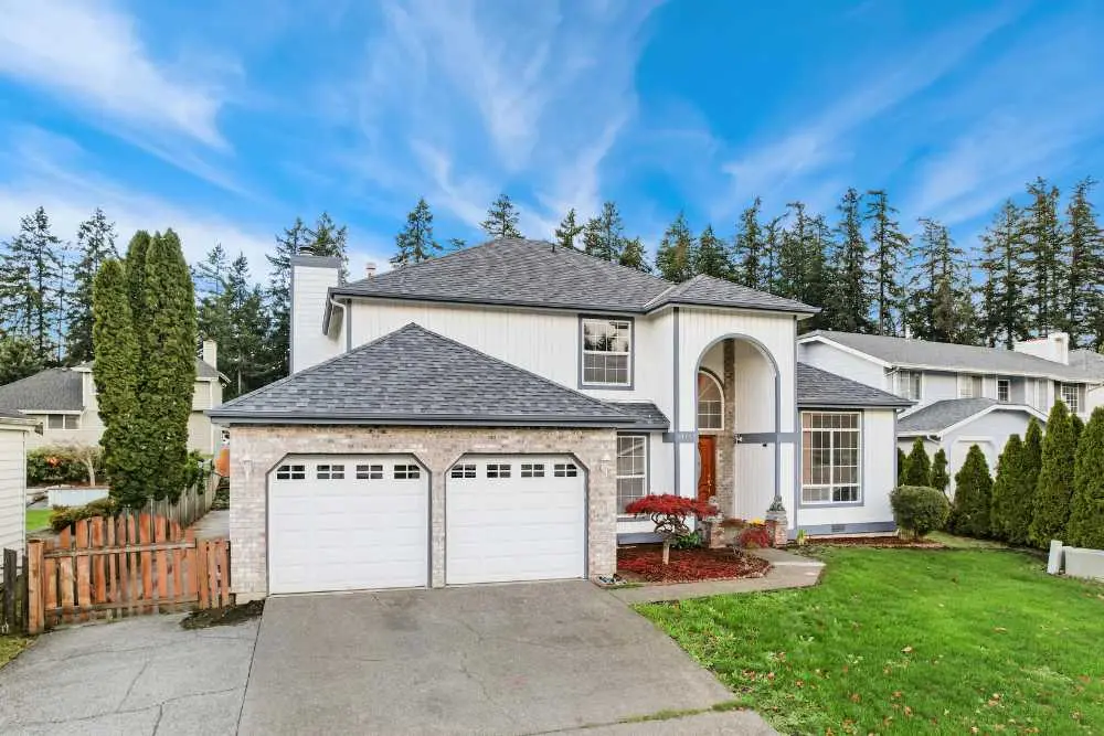 A two-story house with a double garage and a well-maintained lawn is shown under a clear blue sky. This image represents a typical home in need of garage door repair services in Green Bay or Appleton.| Bestland Garage Door Service – Green Bay Garage Door Repair