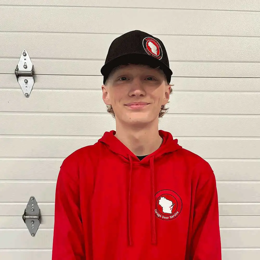 A young technician in a red hoodie with a logo stands smiling in front of a closed garage door, representing Bestland Garage Door Repair services in Green Bay and Appleton.| Bestland Garage Door Service – Green Bay Garage Door Repair
