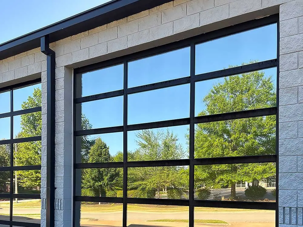 garage-door-34 Modern glass garage doors reflect lush green trees under a clear blue sky. This image exemplifies the quality of garage door repair available in Green Bay and Appleton, highlighting sleek design and expert craftsmanship in residential settings.| Bestland Garage Door Service – Green Bay Garage Door Repair