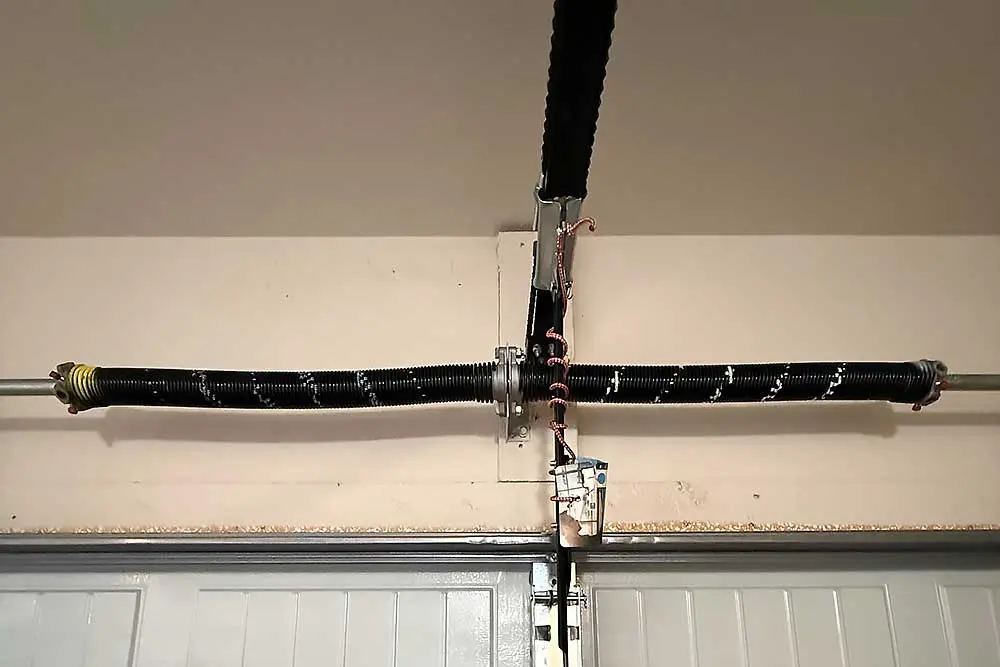 A garage door torsion spring system is shown, highlighting the central rod and coiled springs. This image represents the type of garage door repair services…| Bestland Garage Door Service – Green Bay Garage Door Repair